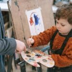 Jak prowadzić zajęcia plastyczne w grupie mieszanej wiekowo: organizacja, materiały, tempo Chłopiec maluje farbami pod okiem nauczycielki na zajęciach plastycznych