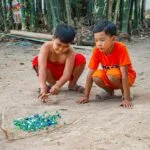 Dwóch chłopców bawi się kulkami na piaszczystym terenie przy bambusach