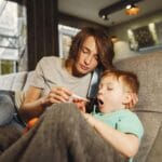 Mama mierzy temperaturę przeziębionemu synowi leżącemu na kanapie
