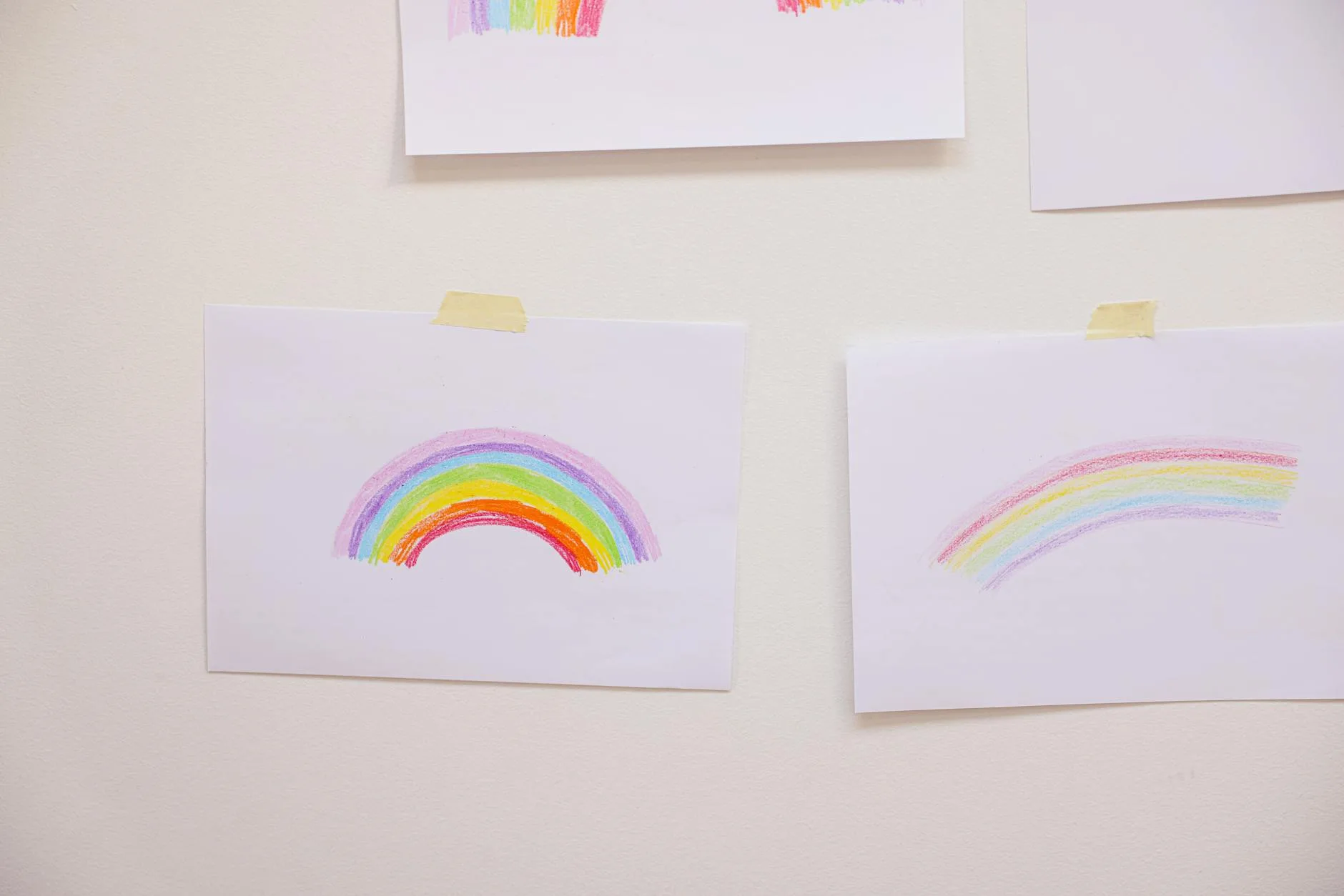 Rysowana kredkami tęcza na kartce przyklejonej do białej ściany