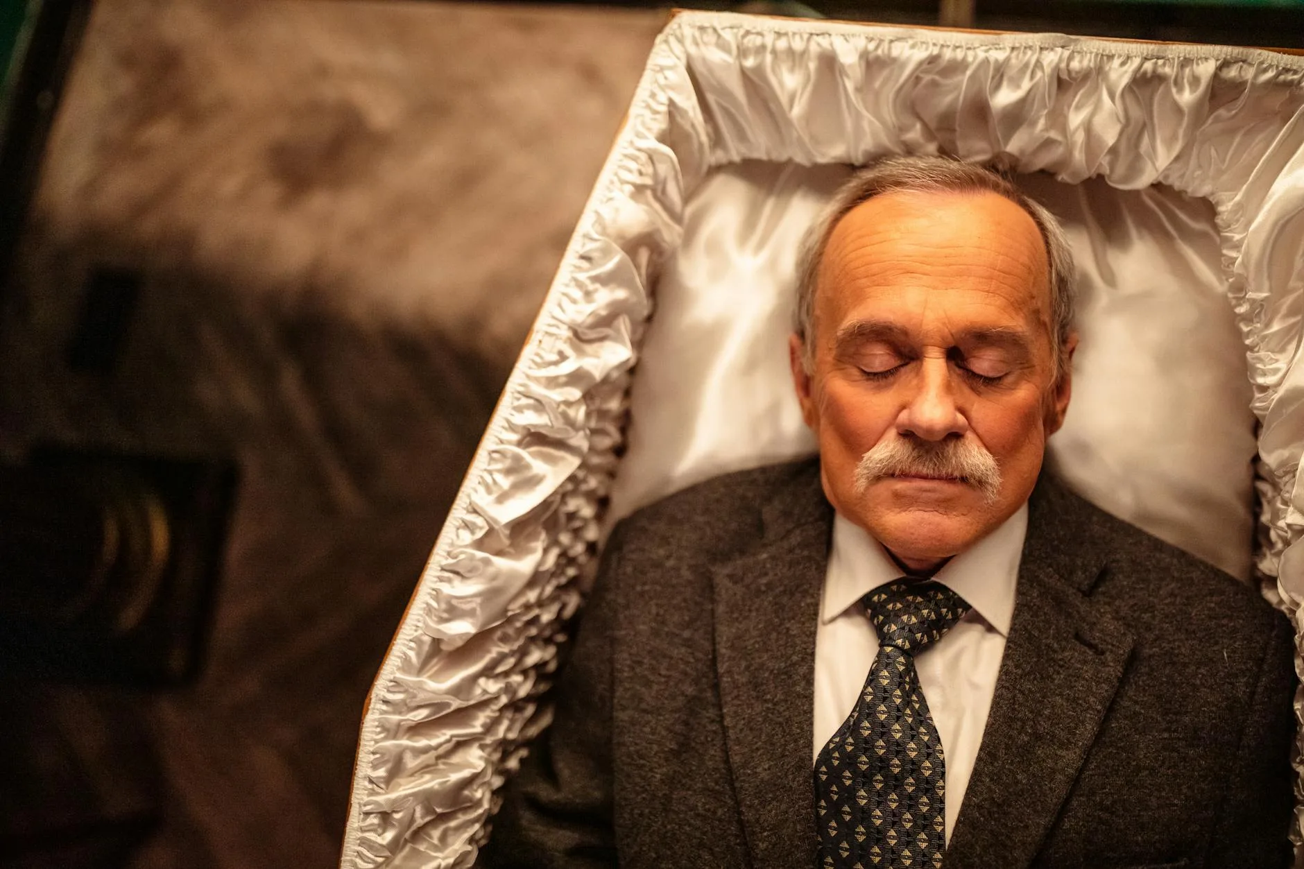 Starszy mężczyzna w garniturze leżący w trumnie, ujęcie z góry