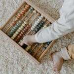 Małe dziecko bawi się kolorowym drewnianym liczydłem na dywanie