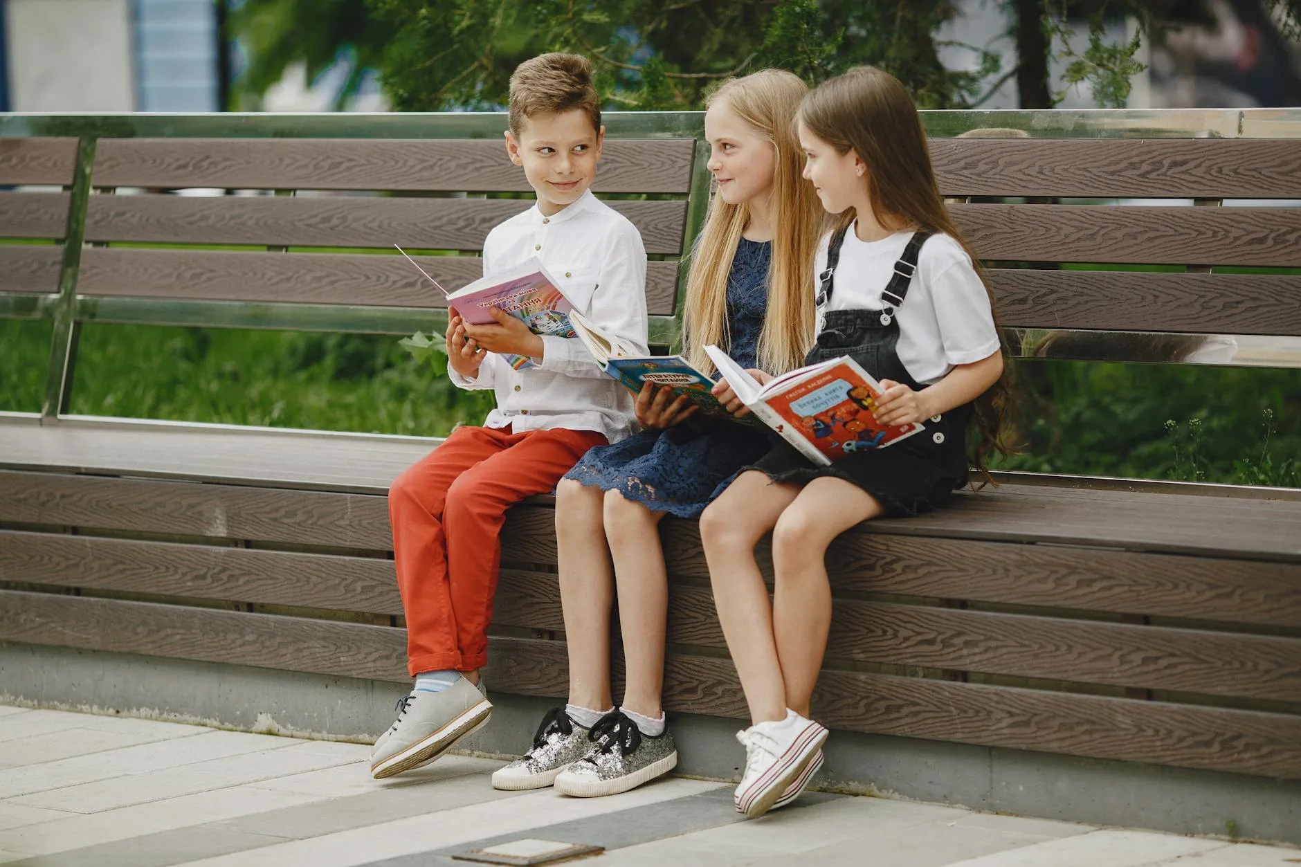 Troje dzieci czyta książki na ławce w miejskim parku